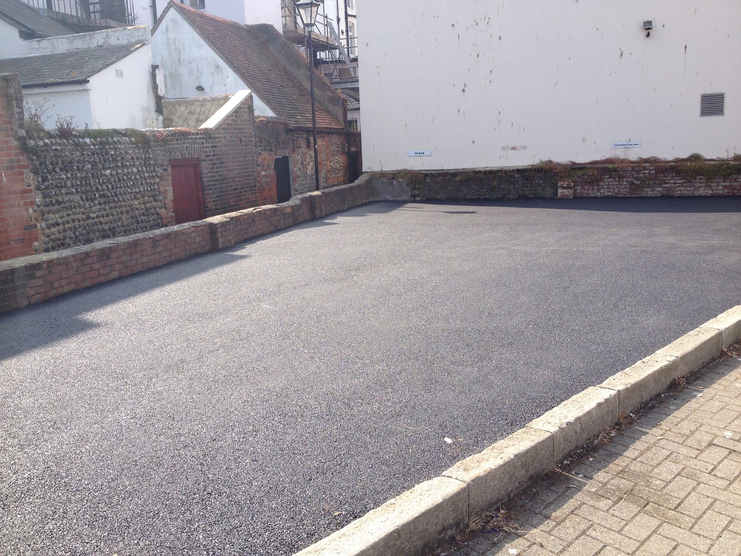 Resurfaced tarmac rear yard enclosed by flint and brick walls